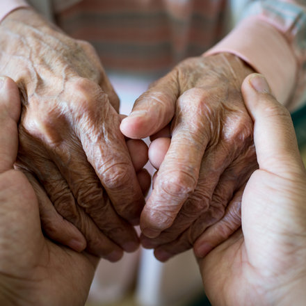 Young hands gently holding the hands of an older adult, symbolizing caregiver support.
