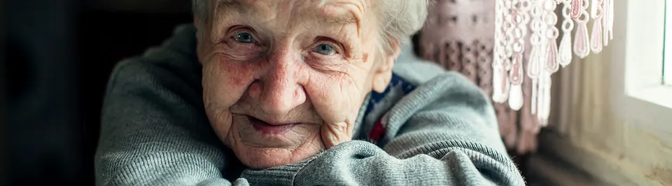 An older woman resting her chin on her hands, smiling